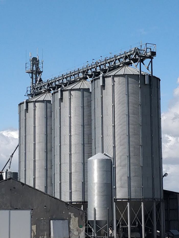 Large metal grain storage silos under a clear blue sky, representing agriculture.
